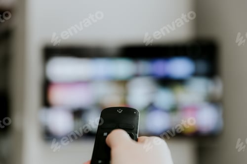 Preview: Hand holding remote control pointing to TV. Person watching smart television