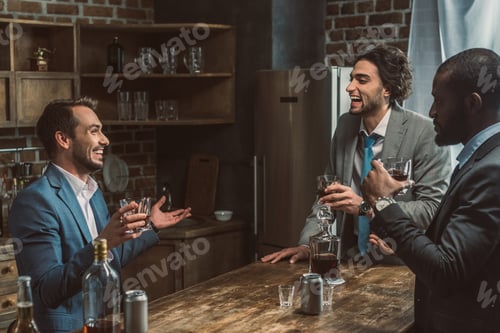 Preview: cheerful young multiethnic men talking and drinking whiskey together