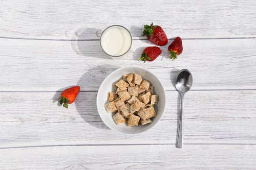 Preview: bowl of cereals with glass of milk and spoon and strawberries from above view