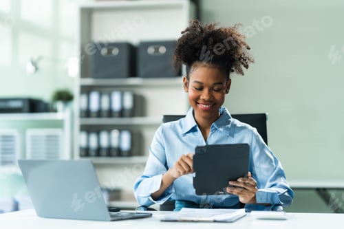 Preview: Utilizing a tablet, a young African American woman in blue formal shirt with afro brown hair works