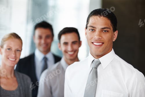 Preview: An african american businessman looking at the camera with his coworkers in the background