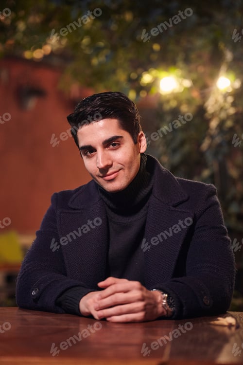 Preview: One Young Handsome Man Portrait, Sitting In Cafe Garden At Table, Night Outdoors, Looking To