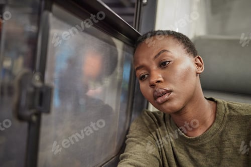 Preview: Cropped shot of a young woman looking depressed while staring out the window of a train