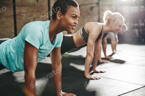 Preview: Smiling young woman doing pushups with friends at the gym