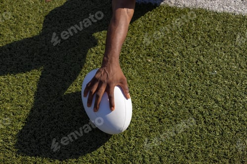 Preview: African American young male athlete holding a rugby ball on grass, copy space