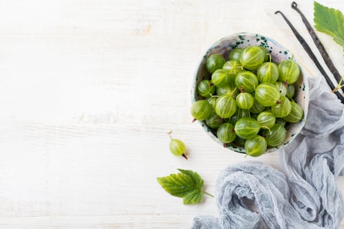 Preview: Fresh raw gooseberry berries in white ceramic plate on light wooden background. Selective focus. Rus