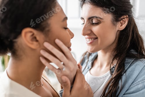 Preview: engaged lesbian woman with wedding ring smiling and hugging multiracial partner