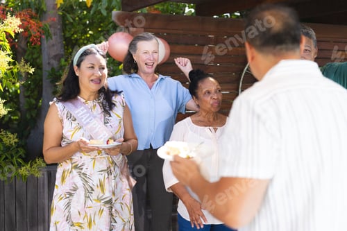 Preview: Celebrating outdoors, diverse group enjoying cake and laughter at birthday party