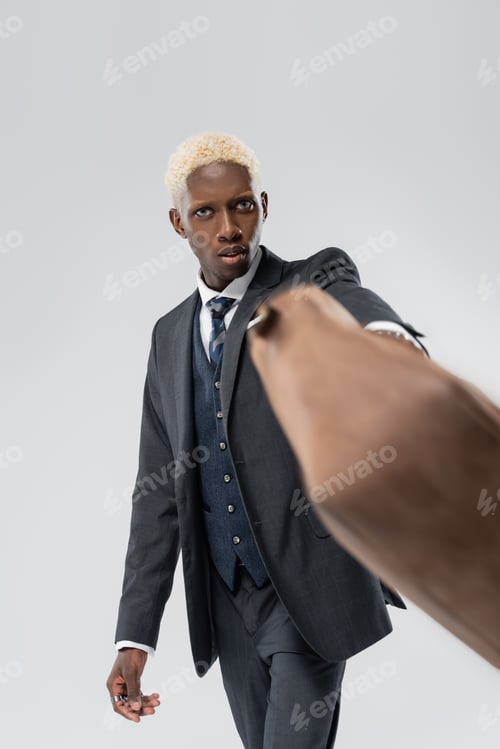 Preview: blonde african american man in suit holding blurred leather bag isolated on grey