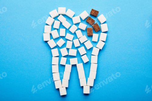 Preview: top view of white and brown sugar cubes arranged in tooth sign on blue background, dental caries