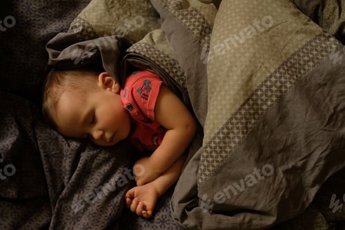 Preview: two years old boy in a red T-shirt sleeps on a bed under a blanket on a pillow