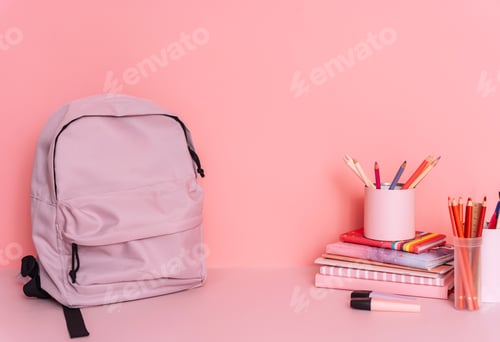Preview: Purple backpack on a table with school supplies in front of a pink background