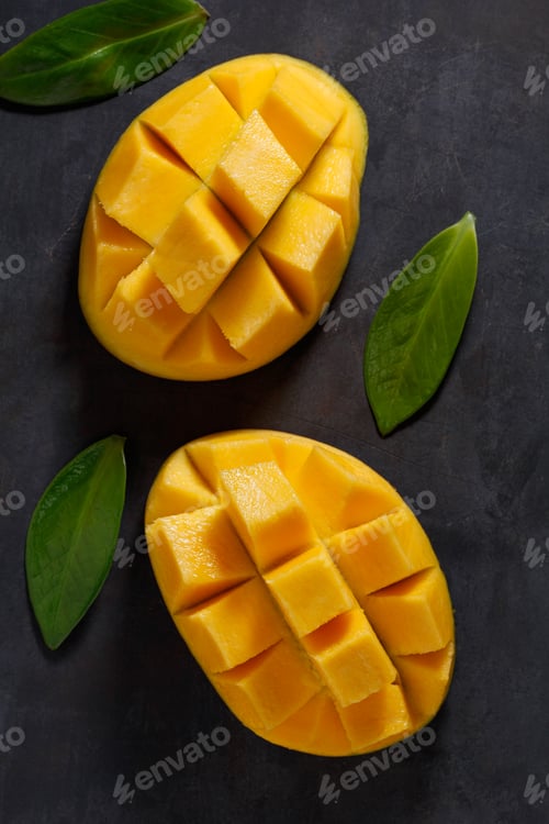 Preview: The two halves of ripe mango on the black textured table. View from above.