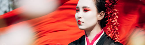Preview: selective focus of tree branches and beautiful geisha with red cloth on background in sunlight,