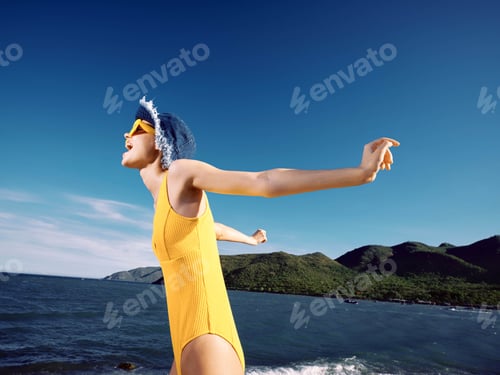Preview: Beach, woman, yellow swimsuit, blue hat, water, mountains a woman in a yellow swimsuit with a blue