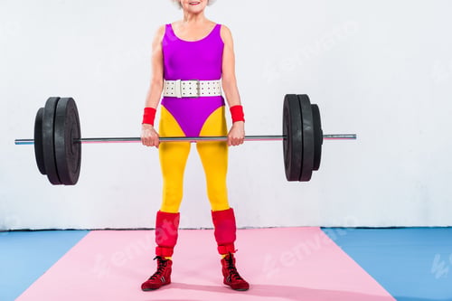 Preview: cropped shot of smiling senior woman in sportswear lifting barbell