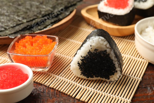 Preview: Tasty tobiko onigiri (Japanese rice ball) and ingredients on wooden table, closeup
