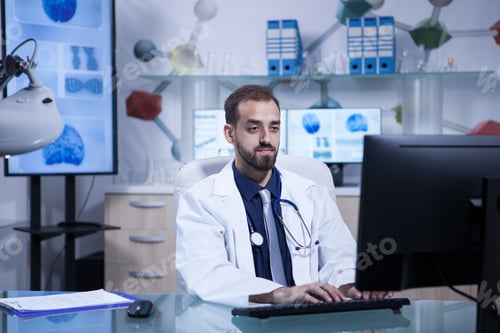 Preview: Portrait of young doctor in white coat working in his hospital office