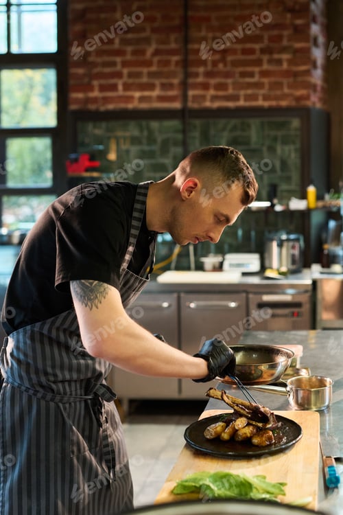Preview: Young Adult Caucasian Man Plating Gourmet Dish in Professional Kitchen