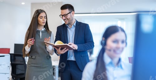 Preview: Business man and business woman walking through office discussing notebook data