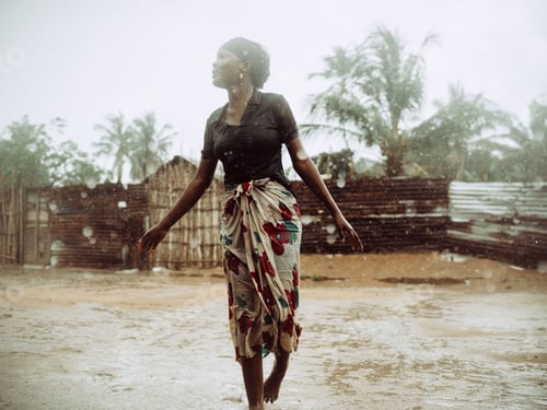 Preview: Young Mozambican woman standing in a muddy field in the rain.