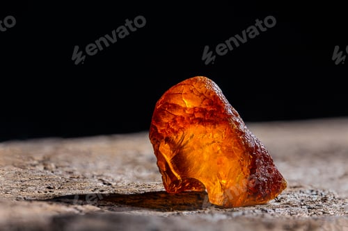 Preview: Natural amber. A piece of yellow transparent natural amber on large piece of dark stoned wood.