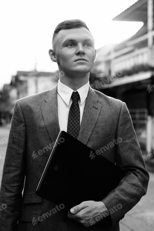 Preview: Young businessman with laptop in the streets outdoors