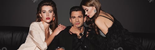 Preview: panoramic shot of attractive and stylish women hugging handsome man isolated on black