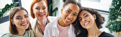 Preview: joyful multicultural female friends looking at camera near motivation couch during psychology