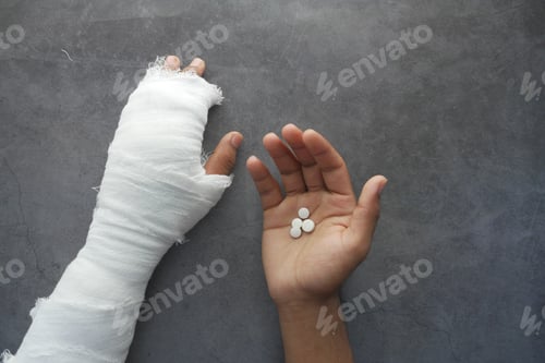 Preview: injured painful hand with bandage and medical pills on hand