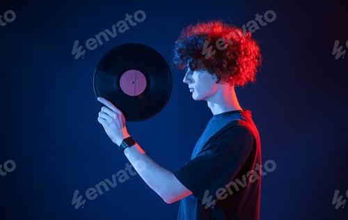 Preview: Musician holding vinyl. Young man with curly hair is indoors illuminated by neon lighting
