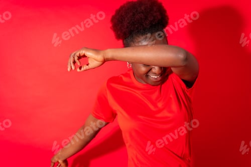 Preview: Young african american woman isolated on a red background smiling and dancing, studio shoot