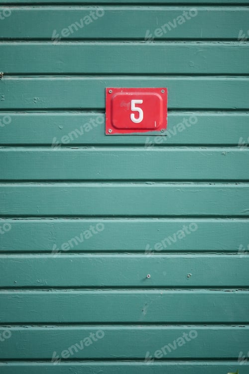 Preview: Number 5 sign on a green wooden wall in daylight