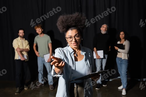 Preview: positive african american woman holding scenario and pointing with hand while rehearsing near