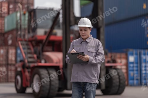 Preview: A logistics worker in a gray uniform inspects stacked shipping containers