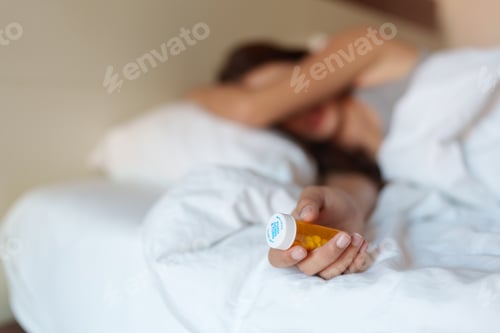 Preview: Sick woman holding medicine bottle while lying in bed