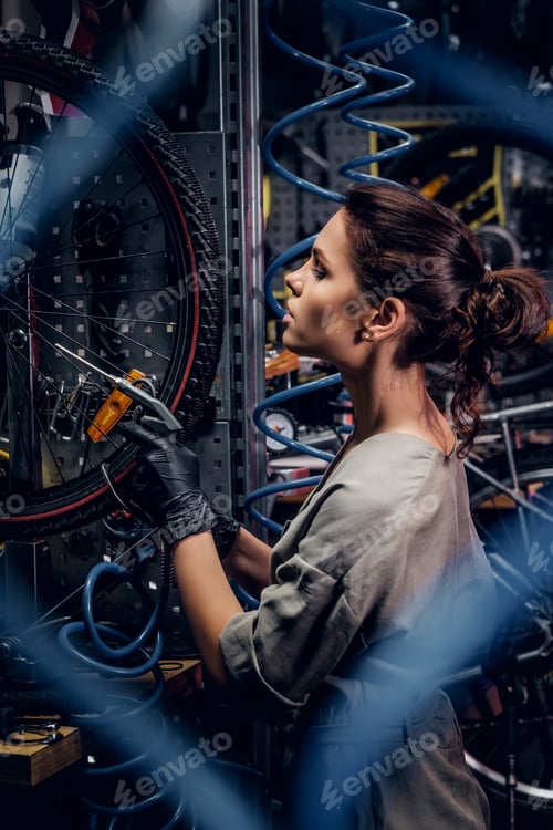Preview: Diligent attractive woman is fixing bicycle at busy workshop in between pneumatic wires