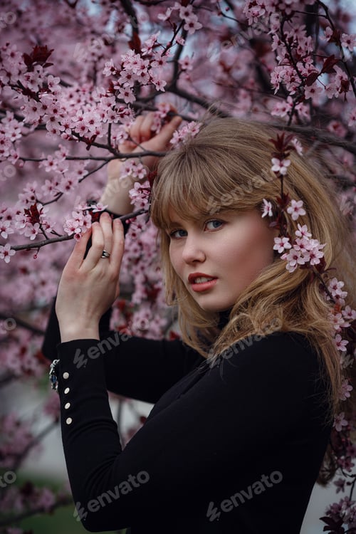 Preview: Outdoor fashion photo of a beautiful young lady in a pink cherry blossom garden.