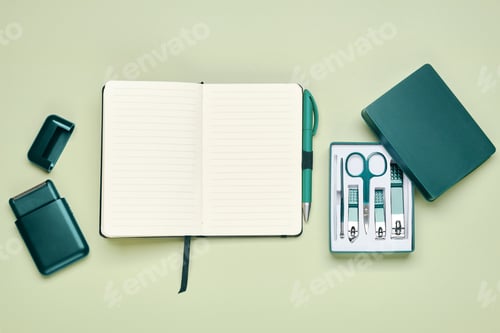 Preview: Top view of a blank notebook, green pen, scissors, nail clippers and electric shaver