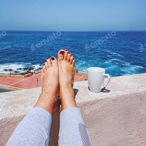 Preview: Coffee break and self-isolation concept. Female barefoot against blue sea and white mug