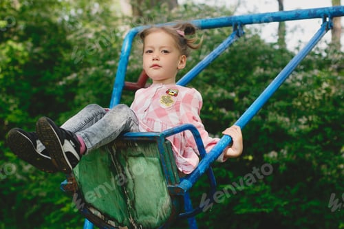 Preview: Serious pretty little girl swinging in the park and looking at camera