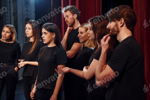 Preview: Side view. Group of actors in dark colored clothes on rehearsal in the theater