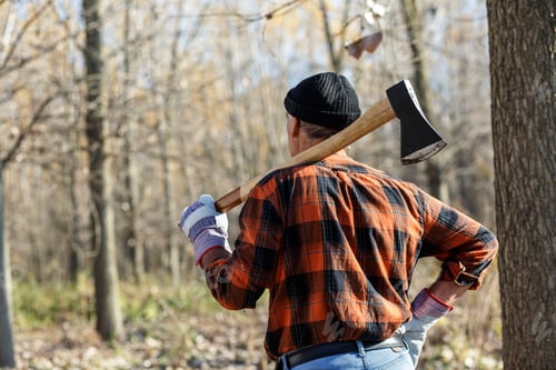Preview: Rear view of senior lumberjack in nature holding an axe on his shoulder.