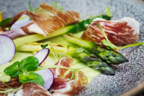 Preview: Close up high angle view of green asparagus and ham on a plate. A restaurant dish.