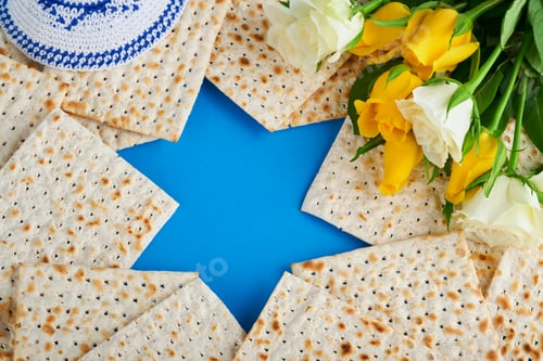Preview: Passover celebration concept. Blue Star of David made from matzah, white and yellow roses, kippah an