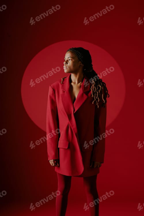 Preview: Contemplating Woman in Red Suit with Braided Hair on Red Backdrop