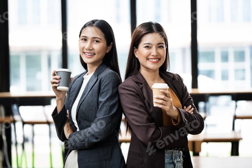 Preview: Two smiling girls have coffee time, standing with arms crossed in co workspace.