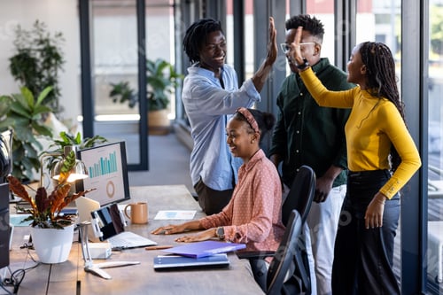Preview: Team celebrating success in modern office, high-fiving near computer with charts
