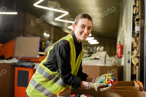 Preview: Young and smiling female sorter in high visibility vest and gloves looking at camera while holding