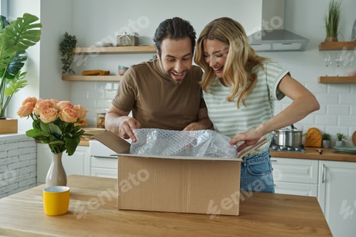 Preview: Curious young couple unpacking box while standing at the domestic kitchen